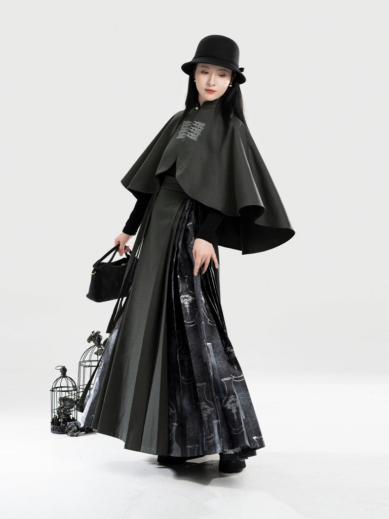 Person wearing a black outfit with a cape and hat, holding a black bag on a white background