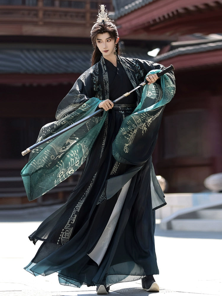 Person in traditional dark and teal outfit with a spear, standing in front of a traditional building.