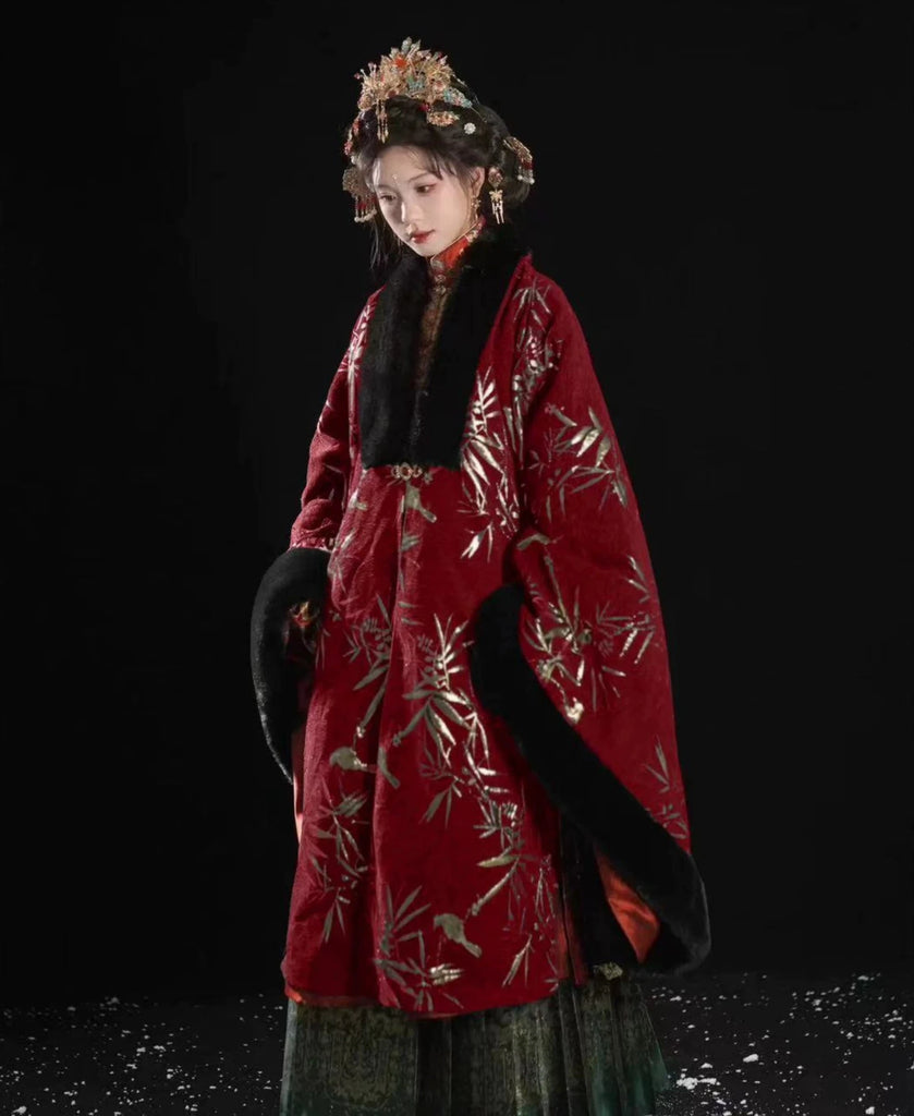 Person wearing a traditional red garment with black fur trim against a dark background