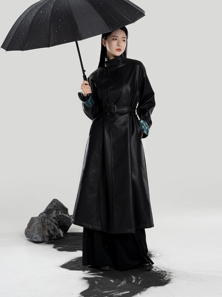 Person wearing a long black coat holding a black umbrella on a white background